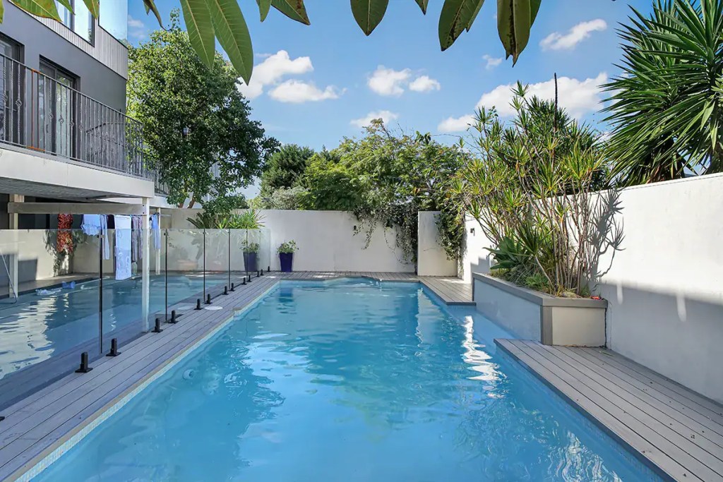 Surface-mounted frameless glass pool fence with matte black hardware finish, installed in a North Curl Curl home.
